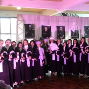 Alunas formandas, reitora e demais autoridades acadêmicas e homenageados posam para a fotografia um ao lado do outro. Todos vestem beca, com exceção do funcionário homenageado. 