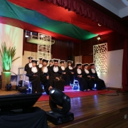14 pessoas sentadas em um palco decorado, vestindo togas azuis e pretas.