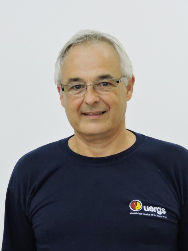 Homem sorridente de pele clara, cabelos brancos e curtos. Usa óculos de grau e veste camiseta azul marinho com o logotipo da Uergs.