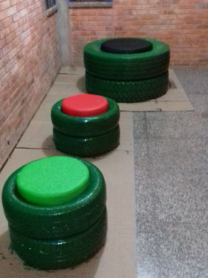 Três sofás feitos de pneus pintados de verde. Ao centro de cada uma deles, estofamento na cor verde, vermelho e preto..