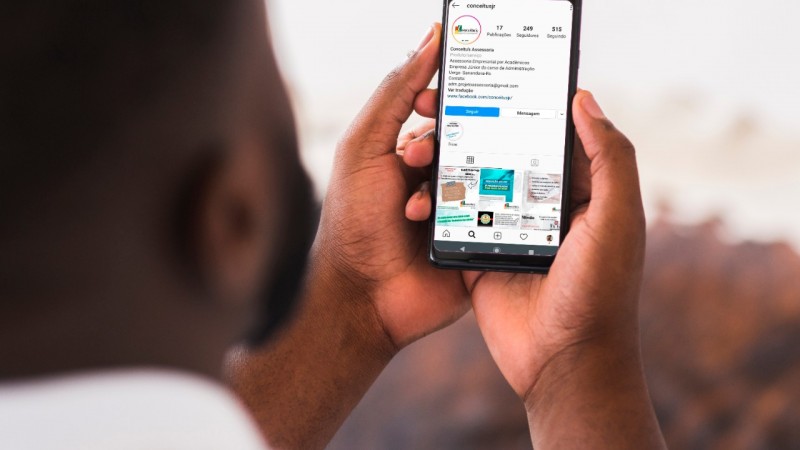 Home segurando celular, onde na tela aparece a página da empresa júnior no instagram.