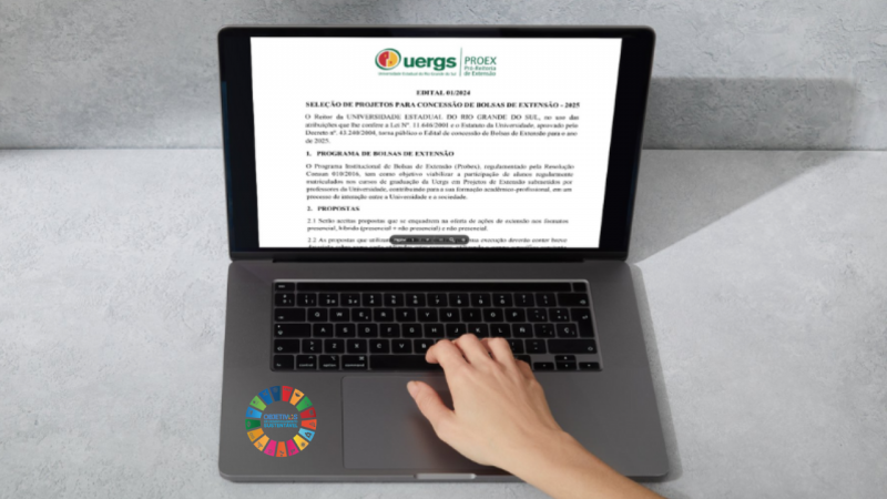 Foto de uma mão de uma pessoa sobre um teclado de notebook. Na tela, há a capa de um documento digital com o título "EDITAL 01/2024 SELEÇÃO DE PROJETOS PARA CONCESSÃO DE BOLSAS DE EXTENSÃO - 2025". Ao lado do teclado, um adesivo com os ODSs.