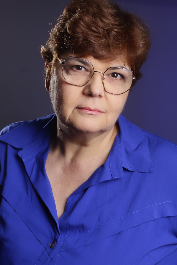 Mulher de pele clara, cabelos castanhos e curtos. Usa óculos de grau e veste camisa azulada.