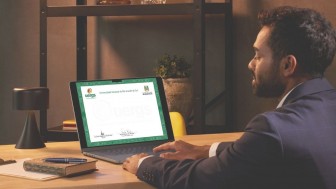Imagem em ambiente interno, com ilumina&ccedil;&atilde;o suave. &Agrave; direita, um homem jovem adulto, de pele clara, cabelos curtos escuros e barba aparada, veste terno escuro e camisa clara. Ele est&aacute; sentado de perfil em frente a uma mesa de madeira, olhando para a tela de um notebook aberto.

Na tela do computador aparece um diploma digital da Universidade Estadual do Rio Grande do Sul (Uergs). No topo do documento est&atilde;o vis&iacute;veis o logotipo da Uergs, o nome &ldquo;Universidade Estadual do Rio Grande do Sul&rdquo; e o bras&atilde;o do Governo do Estado. O diploma possui moldura verde e espa&ccedil;o central claro para as informa&ccedil;&otilde;es do documento.

Sobre a mesa, &agrave; esquerda do notebook, h&aacute; uma lumin&aacute;ria preta, um caderno com capa decorada, um bloco de notas e uma caneta azul. Ao fundo, uma estante escura com prateleiras cont&eacute;m livros e um vaso com planta.